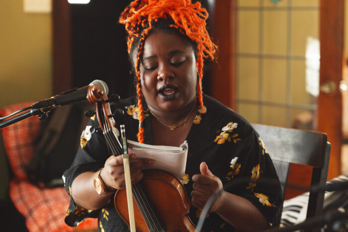Chauntee Ross of SistaStrings with her violin at a microphone