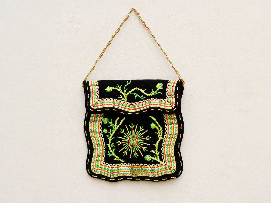 A color photograph of a purse with beadwork. The base fabric is black and the beads are shades of green, yellow, red, and white. There are abstract designs and plant designs.