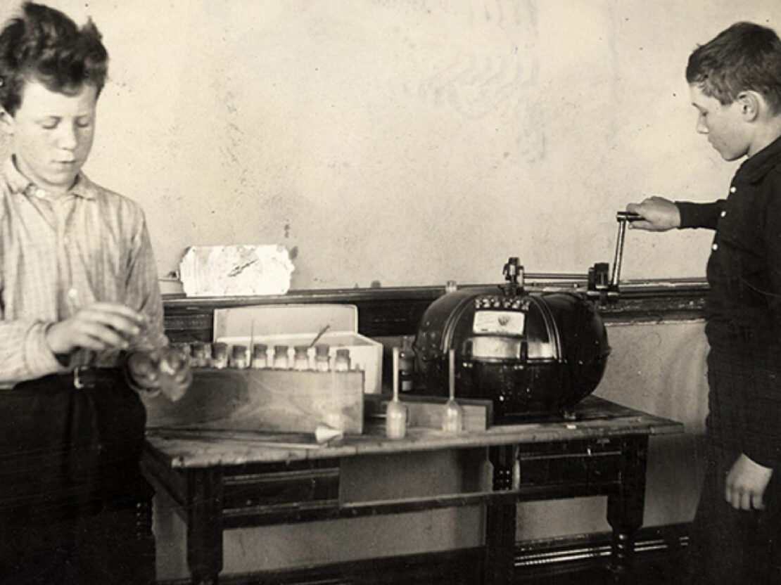 A black and white images of two boys at a tabled experimenting with equipment.