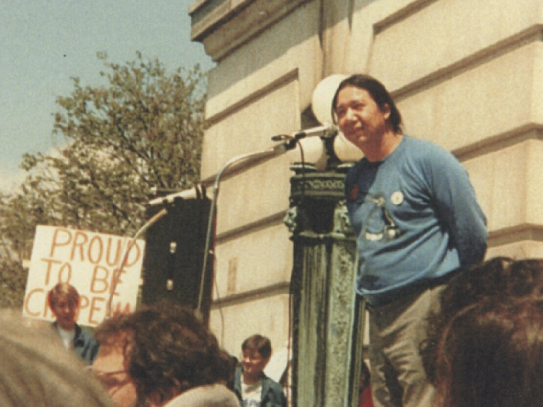 A color photograph of Walter standing at a microphone in front of a limestone building.