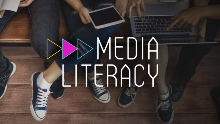The logo for Media Literacy appears in front of a photo of devices like tablets and laptops on the laps of school aged children