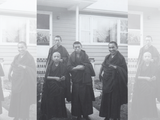 A black and white photograph showing four monks dressed in robes, standing outside of a house.