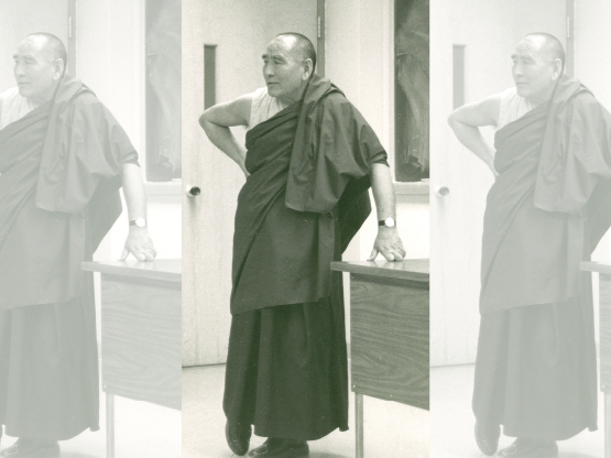 A black and white photograph of Geshe Sopa in his monastic robes standing by a desk. A chalkboard is visible behind him.